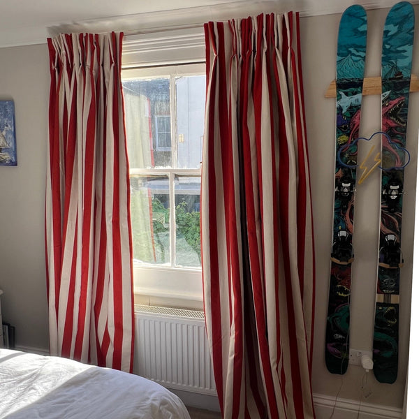 Bespoke printed red and cream cotton linen fabric made into vertically striped curtains hanging on either side of a window in a bedroom.